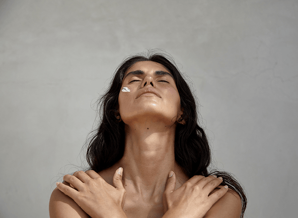 Image of topless womxn closing her eyes with face cream on and arms across chest.