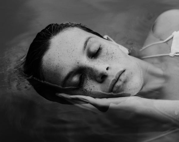 A white woman with freckles with her eyes closed, half submerged in water.