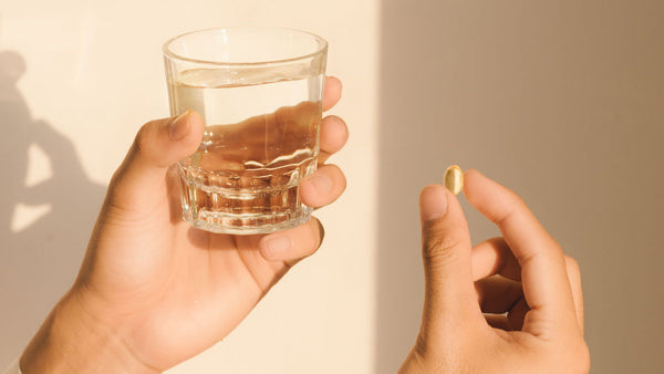 Two hands holding a glass of water and an oil capsule.