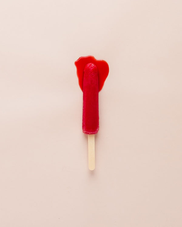 A red popsicle on a pink surface, simulating menstruation.